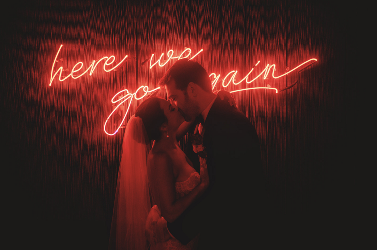 Florida bride and groom share a kiss in the dark in front of red "here we go again" neon sign at Holly Blue venue in Fort Lauderdale