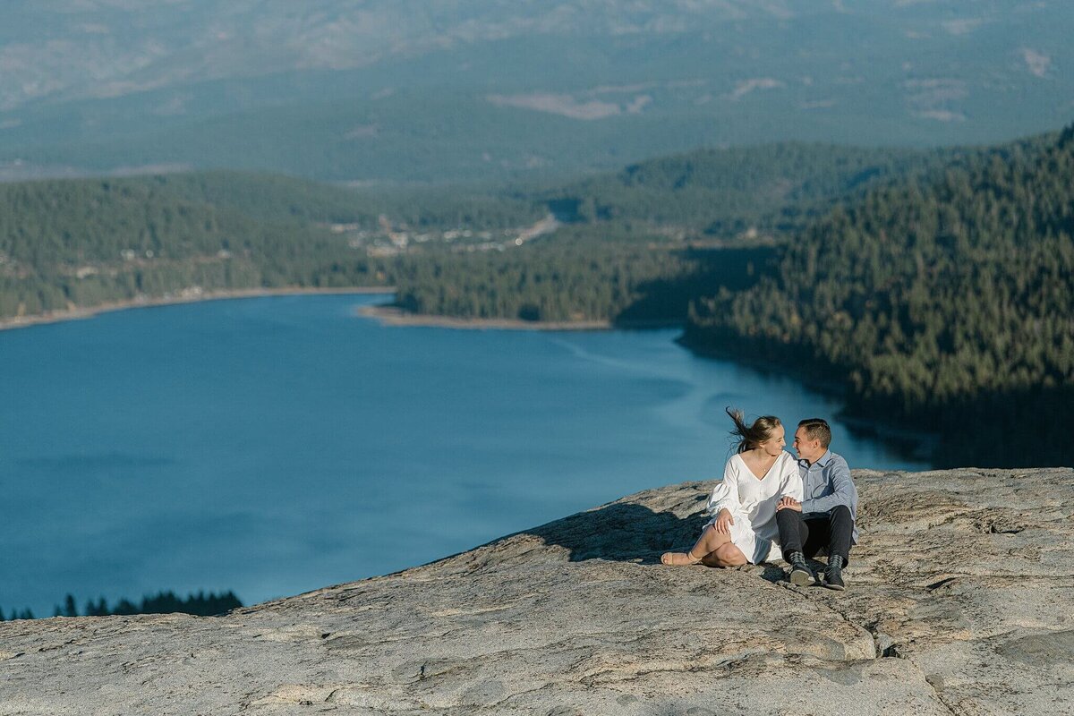 a cozy moment before sunset during an enageement session on Donner Summit with Donner Lake in background. Couple sitting on the granite rocks.