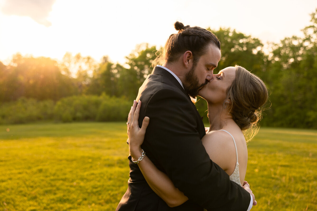 Groom and bride share a kiss during a golden hour sunset at their wedding day reception. Photo taken by Aaron Aldhizer