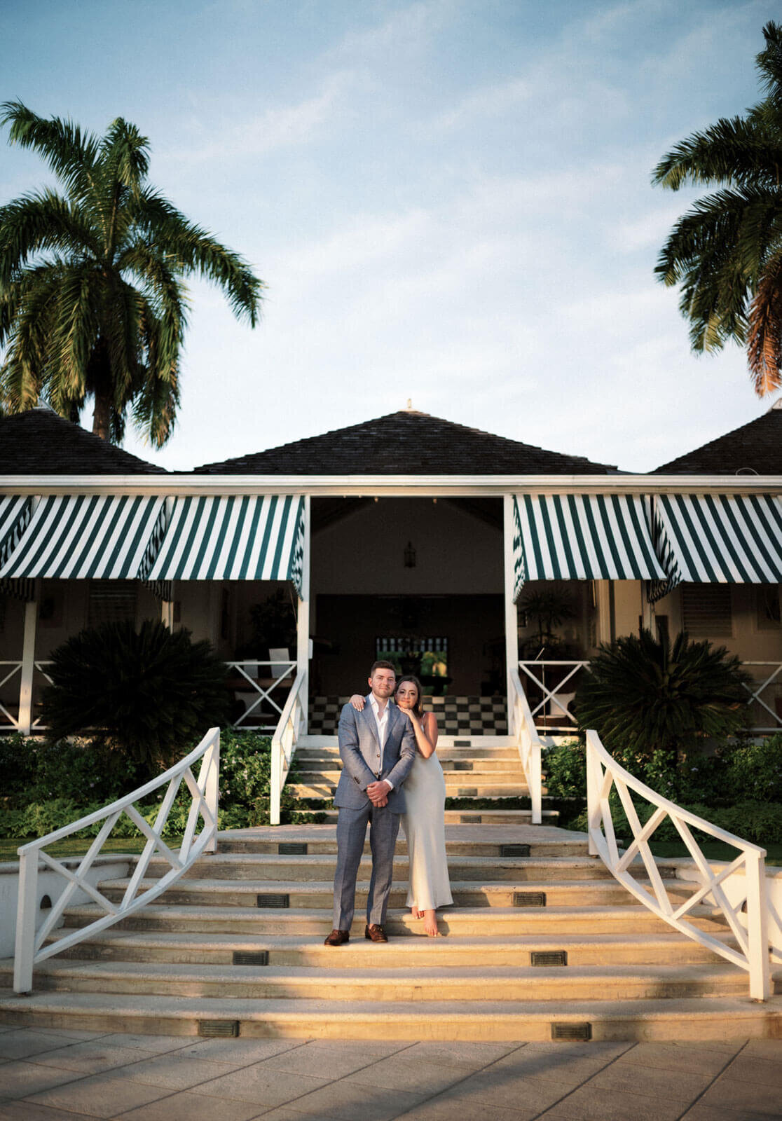 The engaged couple is standing on the staircase that leads to the entrance of Round Hill Hotel and Villas, Jamaica.