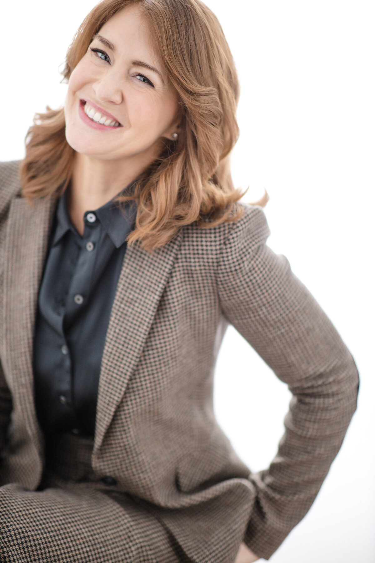A woman in a blazer with her hand on her hip smiling.