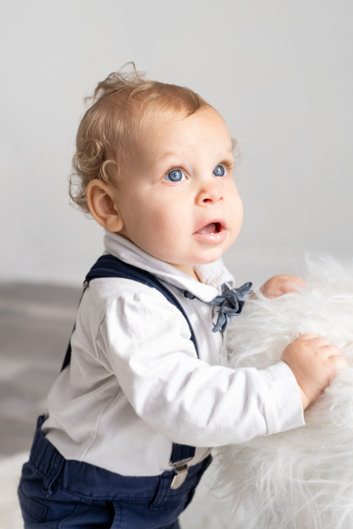 A one year old baby holds onto a stool and stand on his own