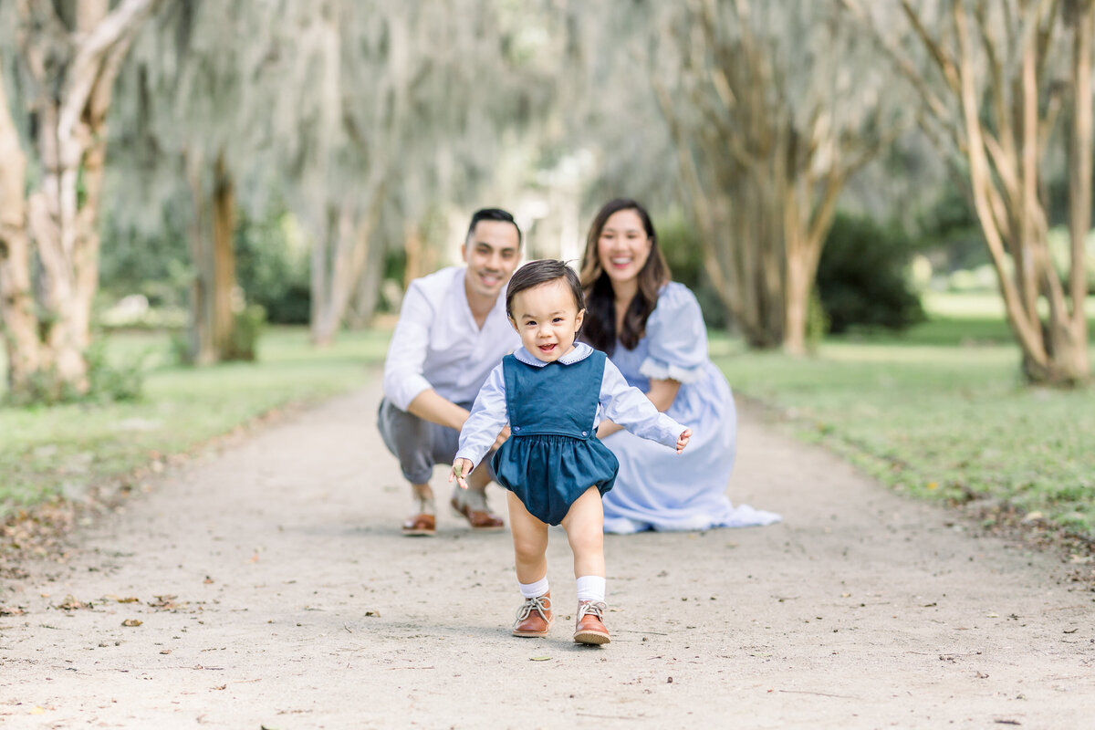 Couple watches baby walk for an outdoor family portrait in White Point Garden , South Carolina.
