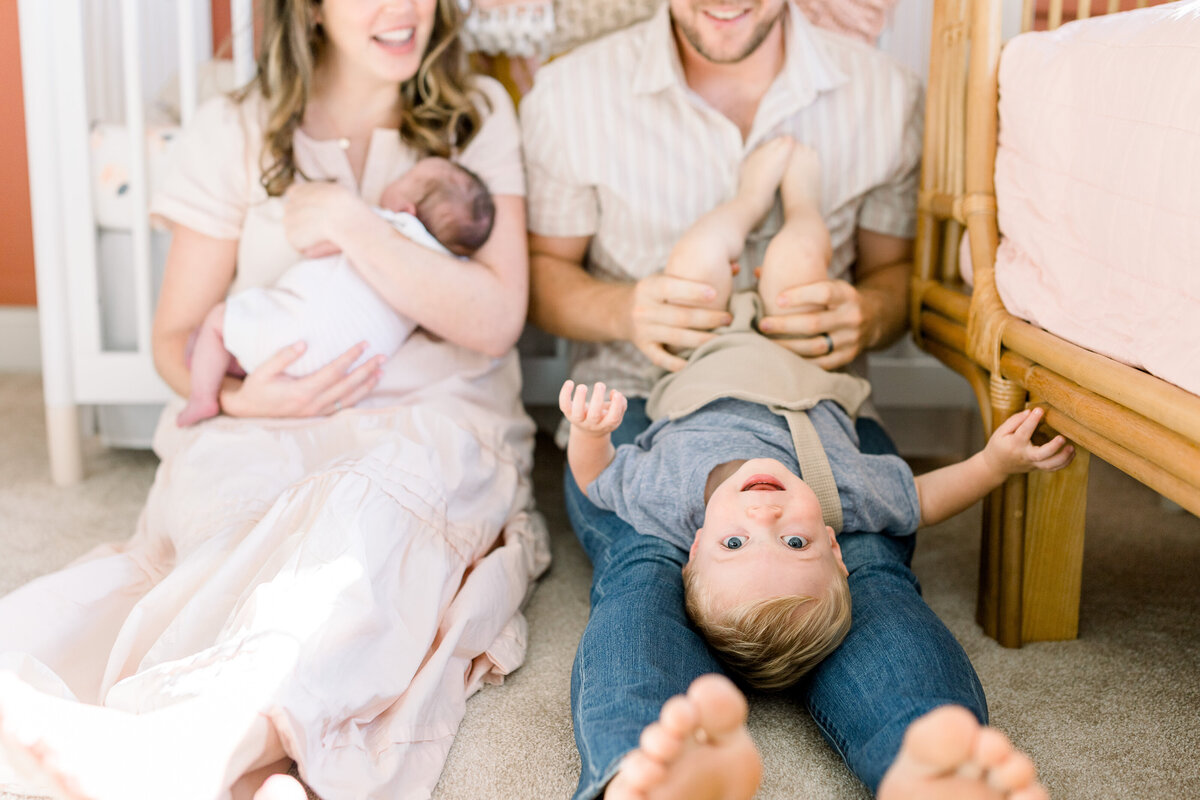 Growing family playing with older child while holding new baby