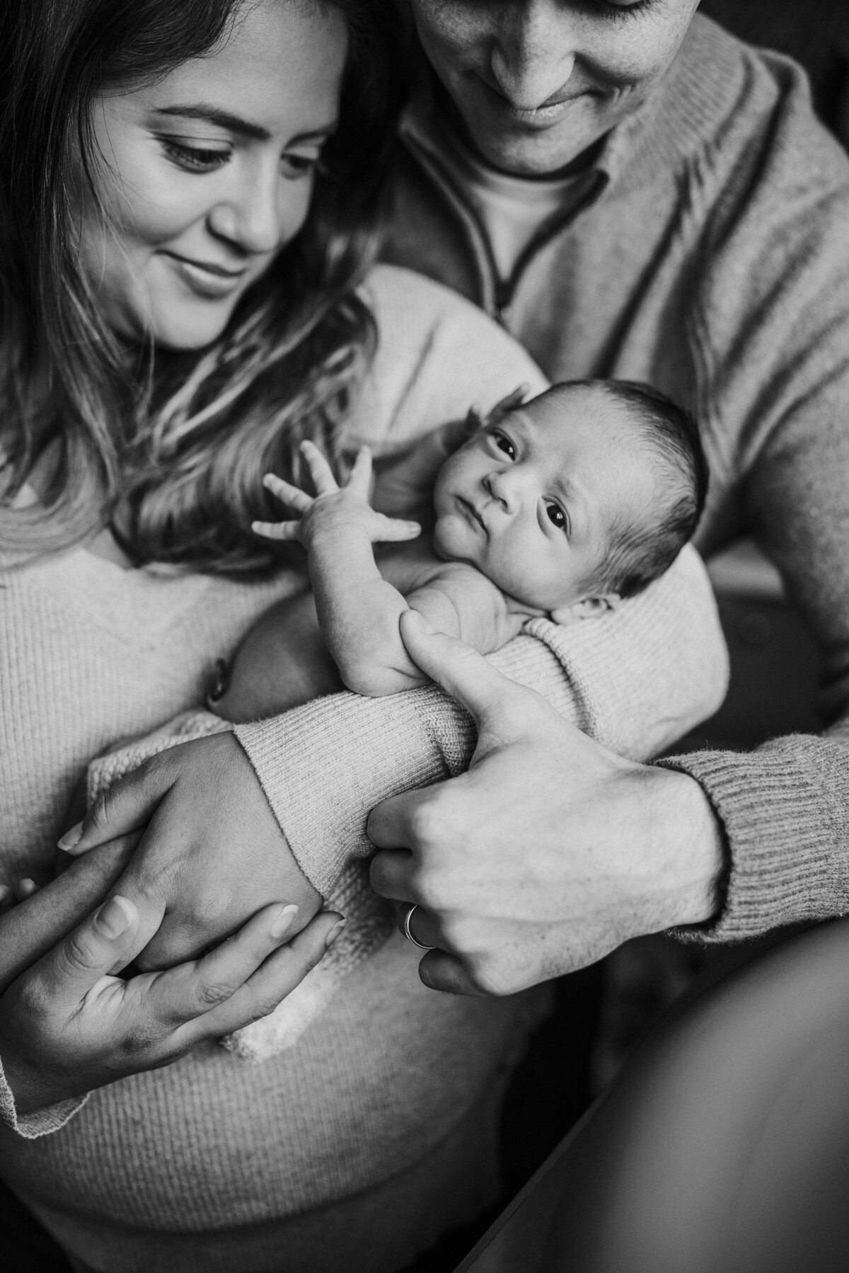 black and white image of new family holding their new baby boy in their arms as baby stares at the camera