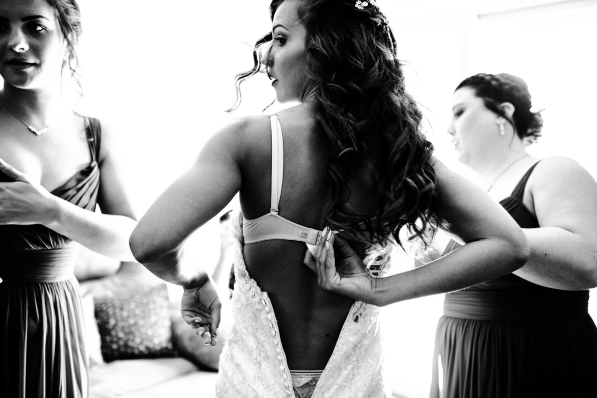 One of the top wedding photos of 2020. Taken by Adore Wedding Photography- Toledo, Ohio Wedding Photographers. This photo is of a bride removing her bra while getting her wedding gown put on in Detroit Michigan.