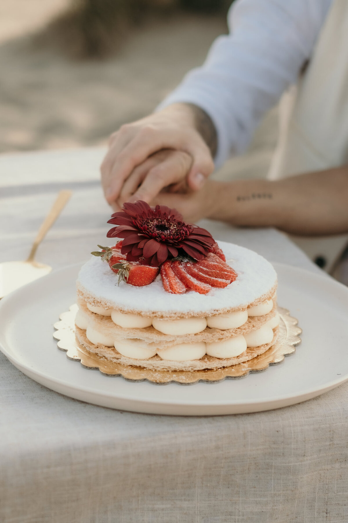 Das Hochzeitspaar schneidet einen kleinen Naked Cake an, der mit Erdbeeren und einer roten Blüte dekoriert ist.