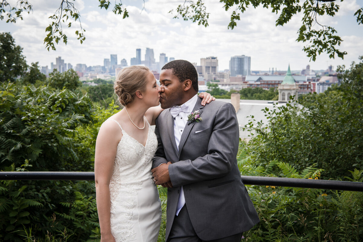 Black groom and bride kiss in front of Saint Paul city.