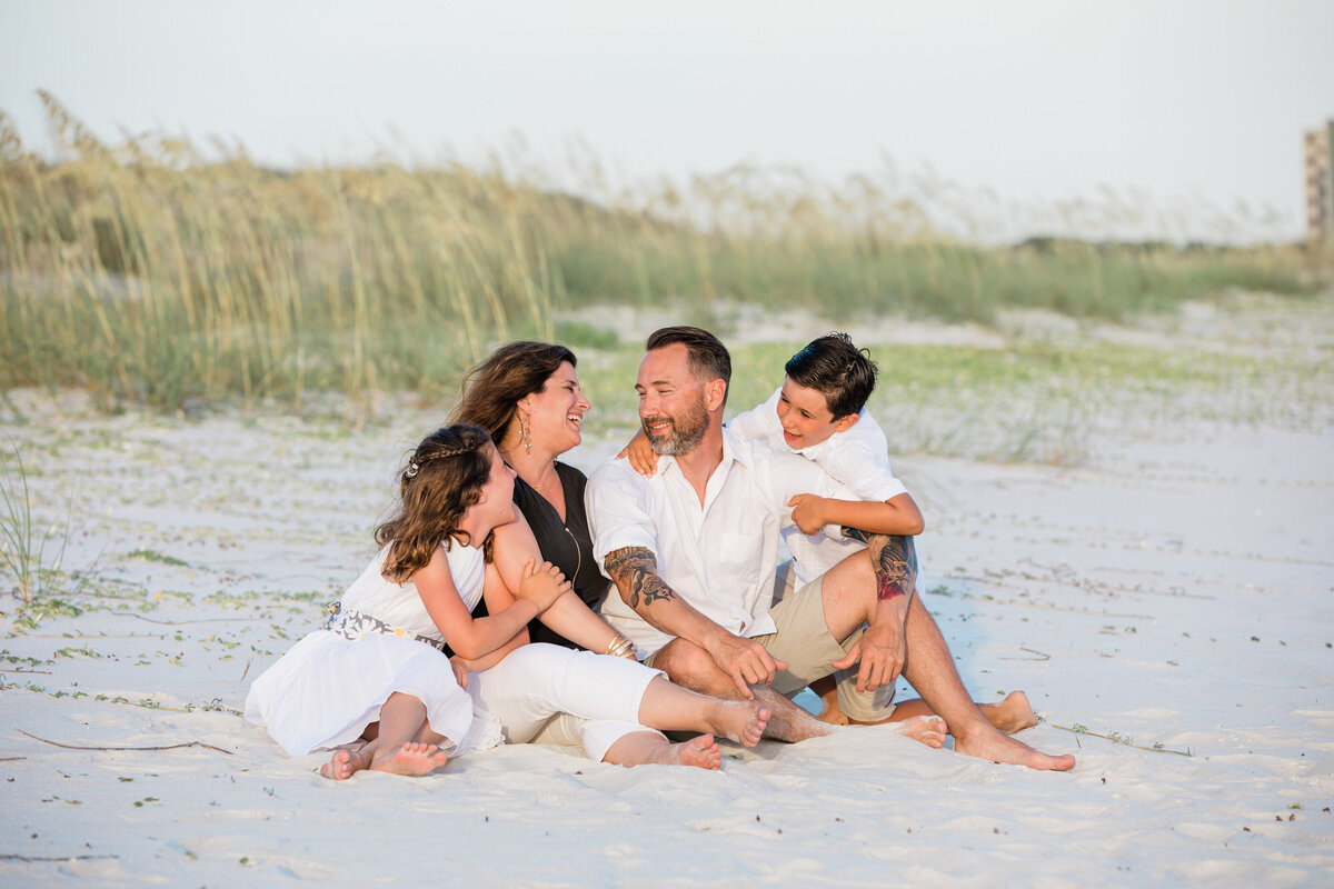 A family of four sitting in the sand together