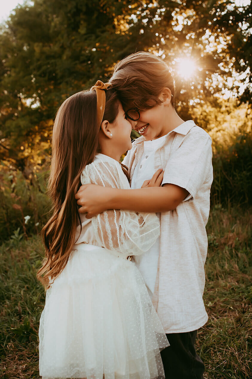 a brother and sister hug nose to nose at sunset in a field