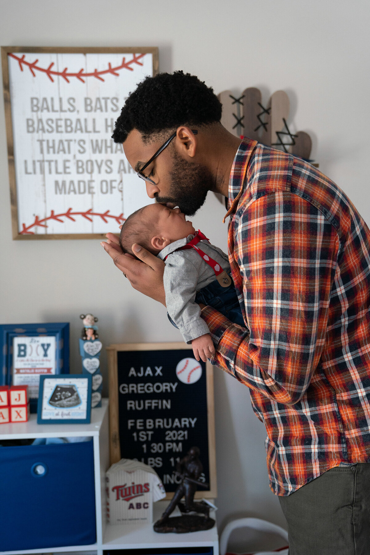 Black man dressed in flannel kisses newborn baby on head in nursery.