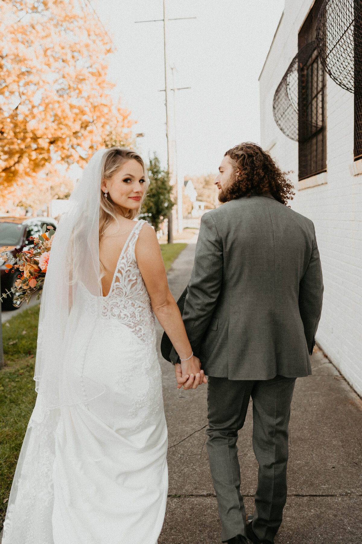 Bride looking over shoulder at camera holding grooms hand