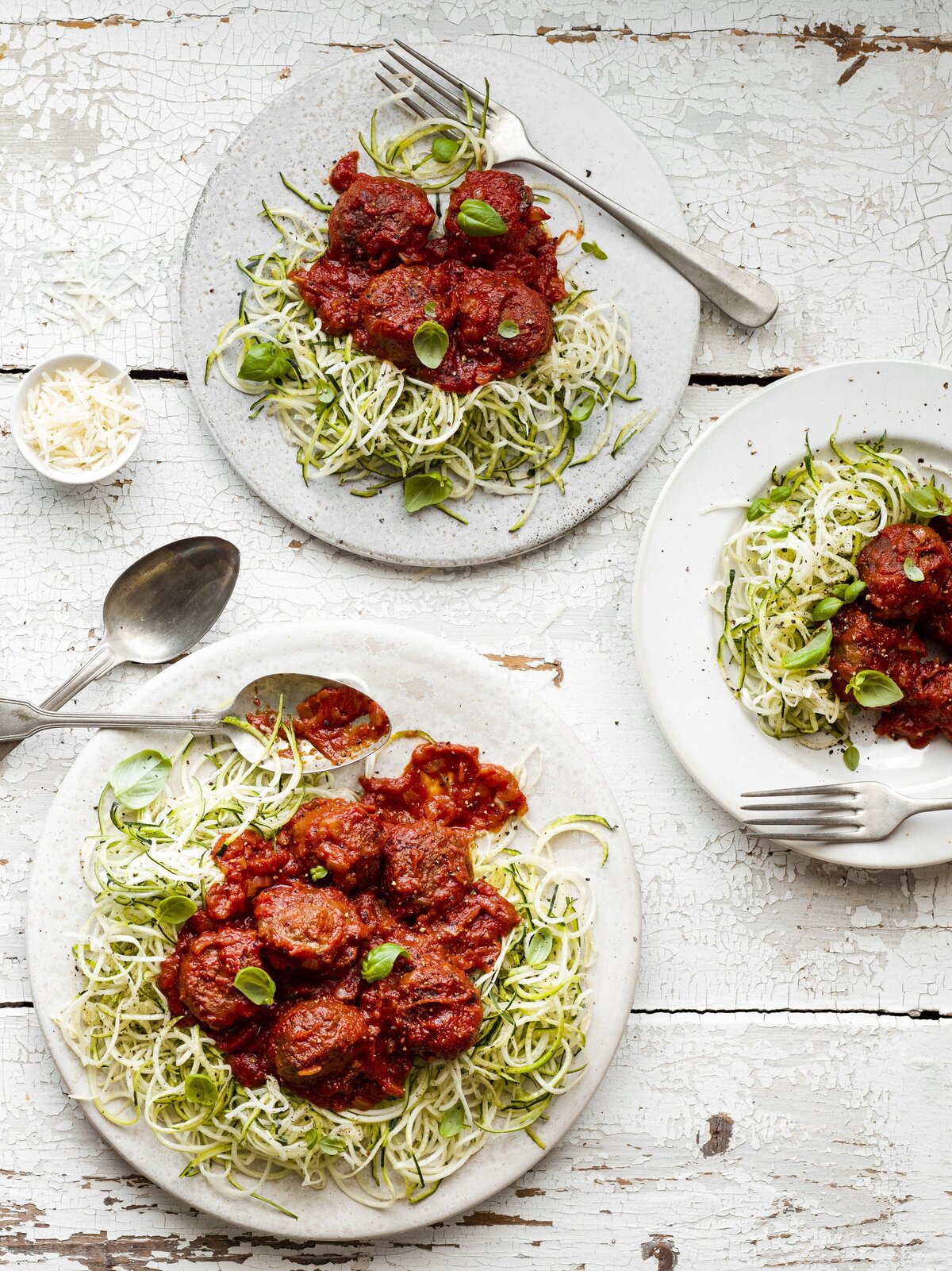 Three plates of zucchini pasta with sauce on top.