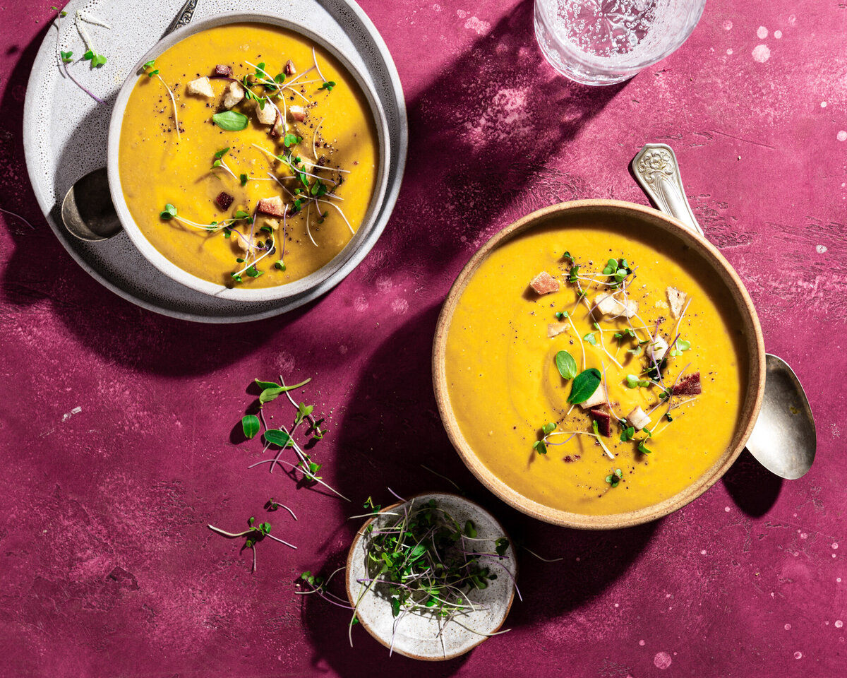 Omayah Atassi Dubai Food Photographer and Food Stylist -- Hard light overhead shot of 2 bowls of lentil soup on a purple backdrop, styled with microgreens
