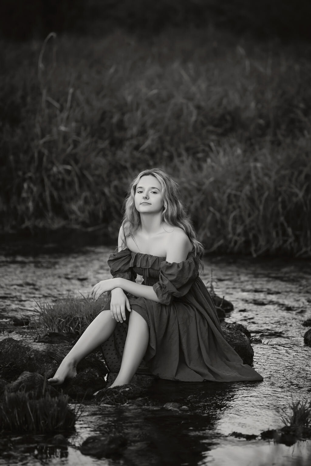 A young woman sitting in the river, with warm light illuminating her serene expression and flowing hair, captured by a Bemidiji, Minnesota fine art senior photographer