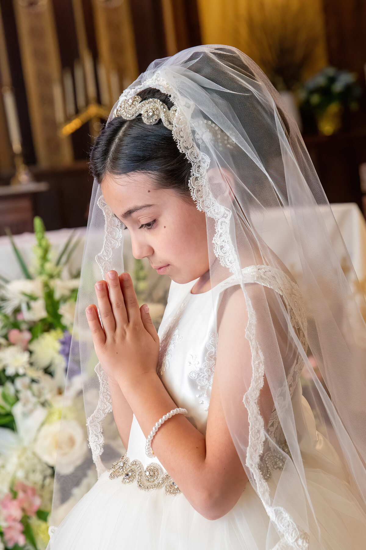 A little girl wearing a First Communion dress and veil folds her hands to pray First Communion mini-session