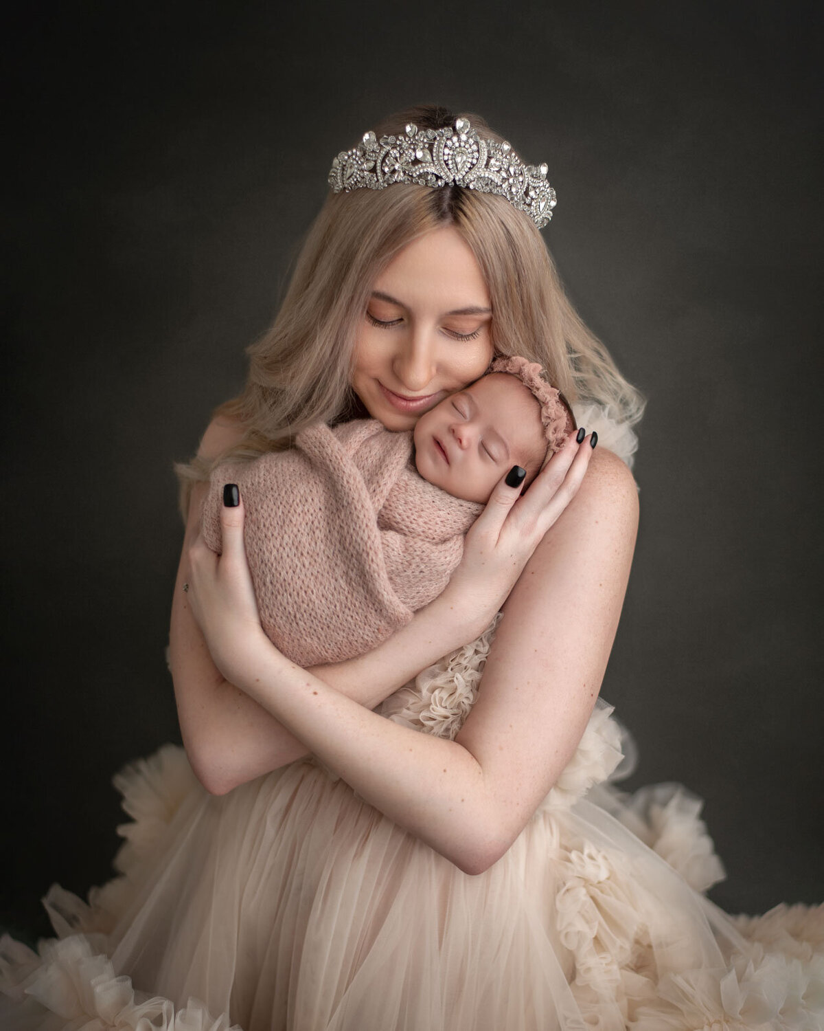 mom in gown with tiara snuggling her newborn daughter