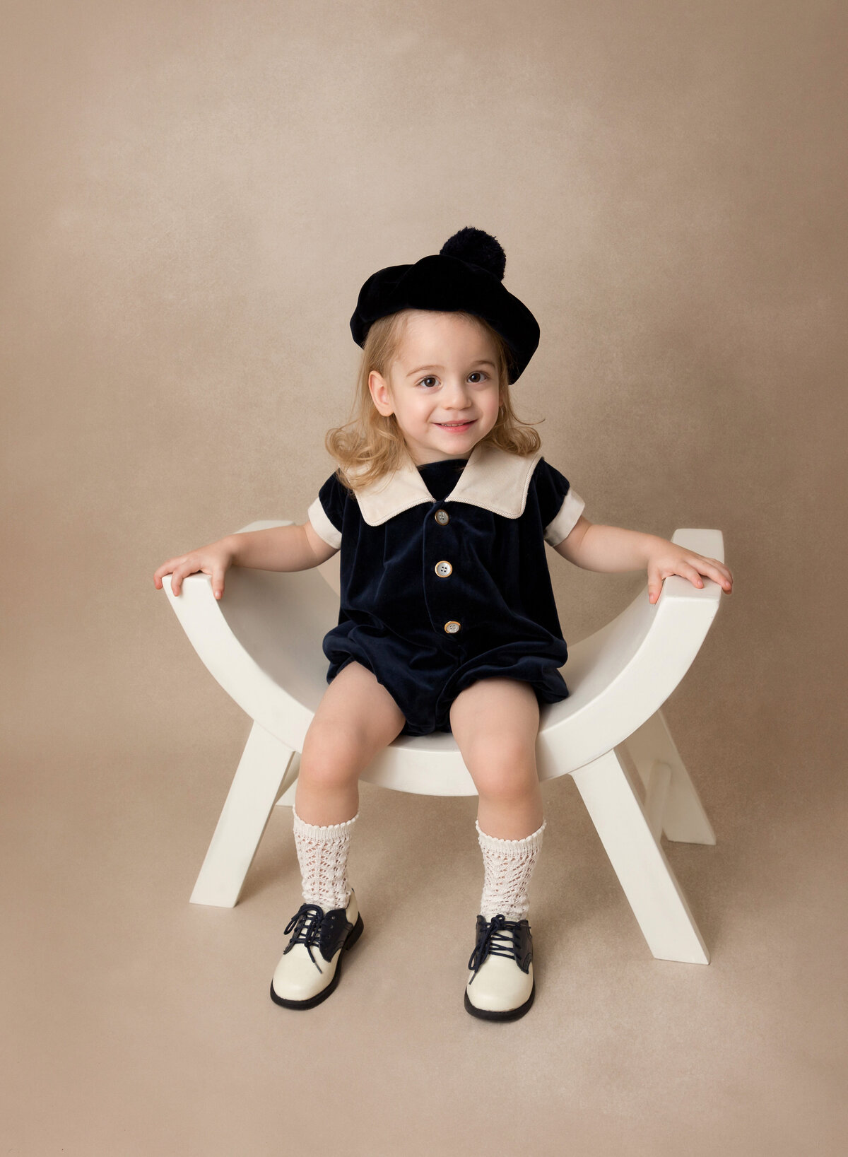 Toddler girl sitting on a char for a milestone portrait. She is smiling at the camera.