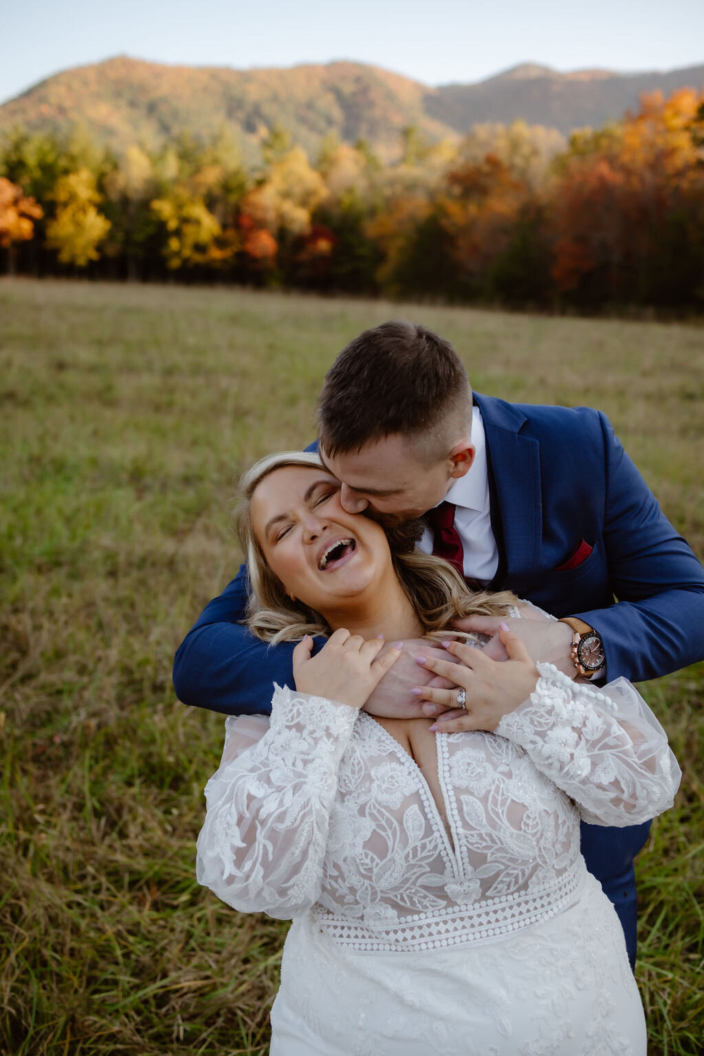 candid wedding photo of groom kissing his bride on the neck as she throws her head back and laughs in Cades Cove photographed by photographers in gatlinburg tn