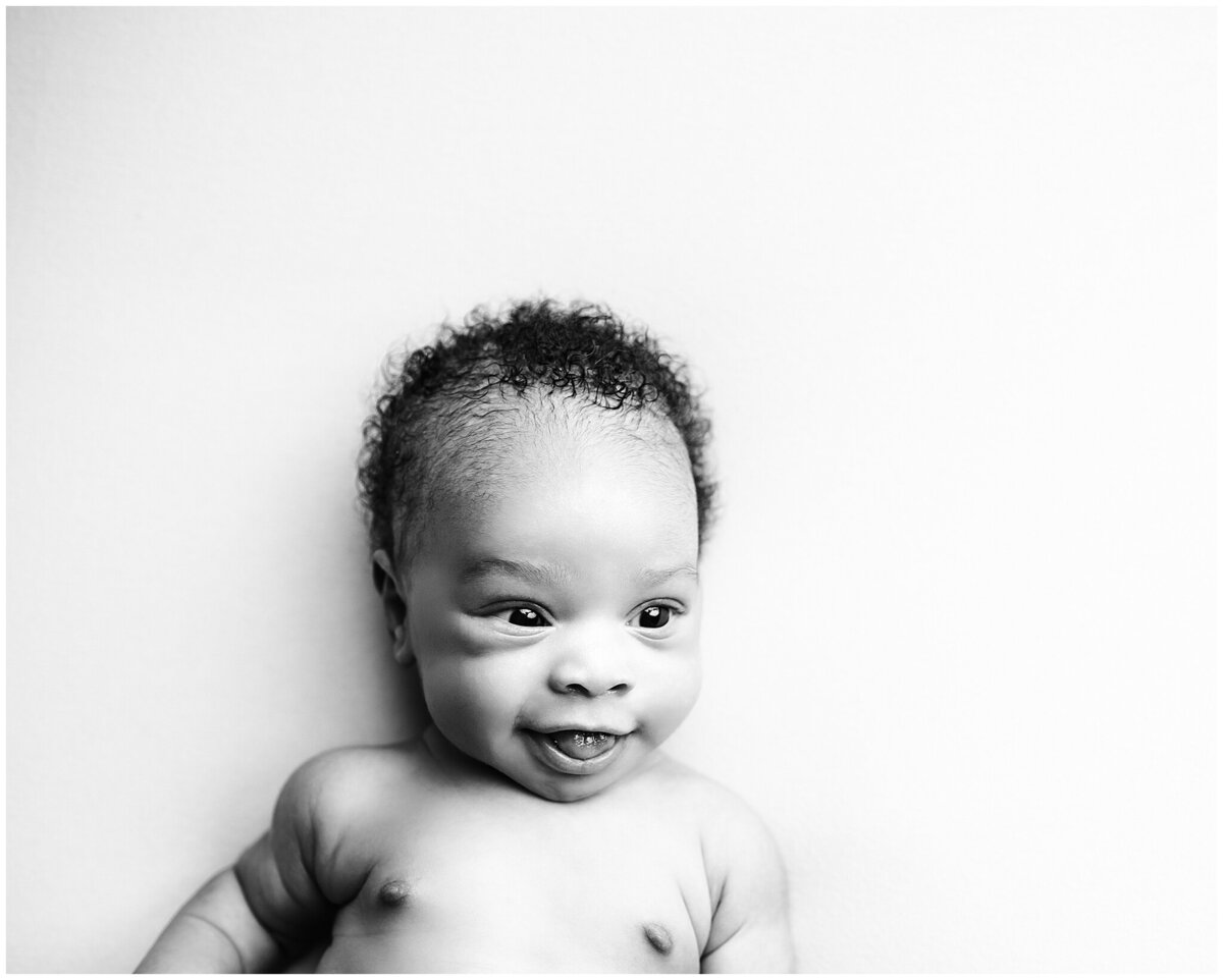 Black and white photo of baby looking around and smiling big.