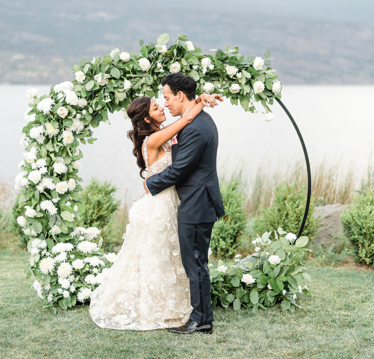 bride and groom embrace in front of a wedding arch.