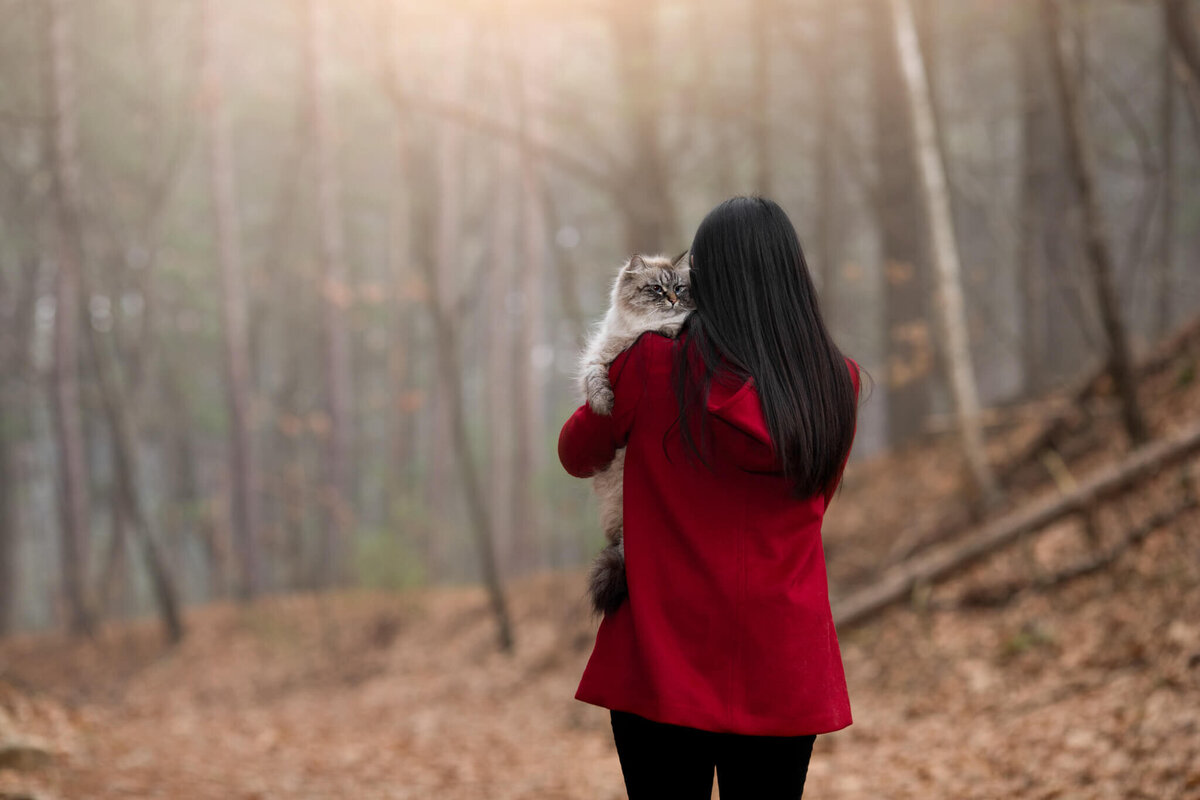 Cat Mom with long black hair facing away with fluffy grey cat over her should looking at the photographer