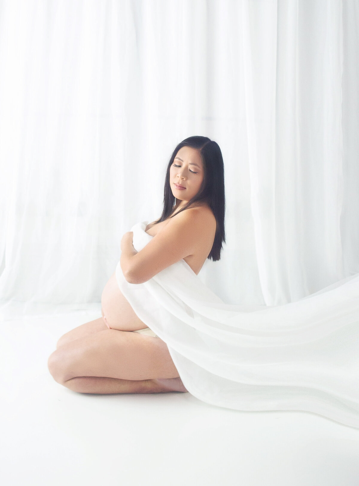 Women with white fabric draped over pregnant belly during maternity photoshoot in Mount Juliet Tennessee photography studio