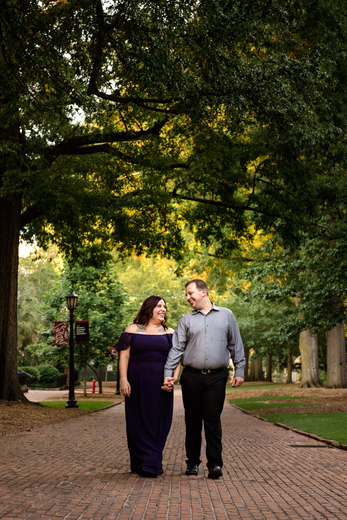 Engaged-couple-walking-toward-the-camera-looking-at-one-another-smiling-in-the-horseshoe-of-the-University-of-South-Carolina