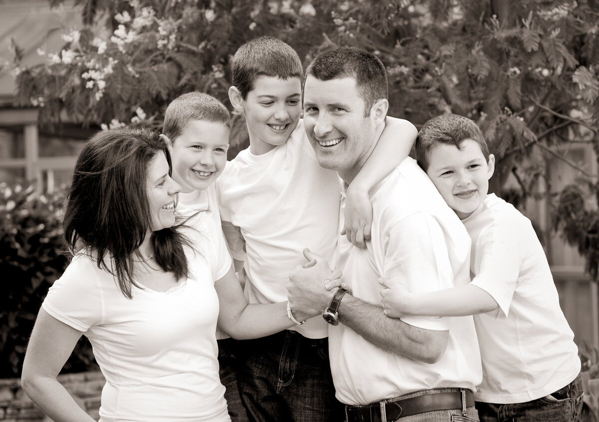 black & white portrait of family of five with brunette hair, wearing white tops smiling
