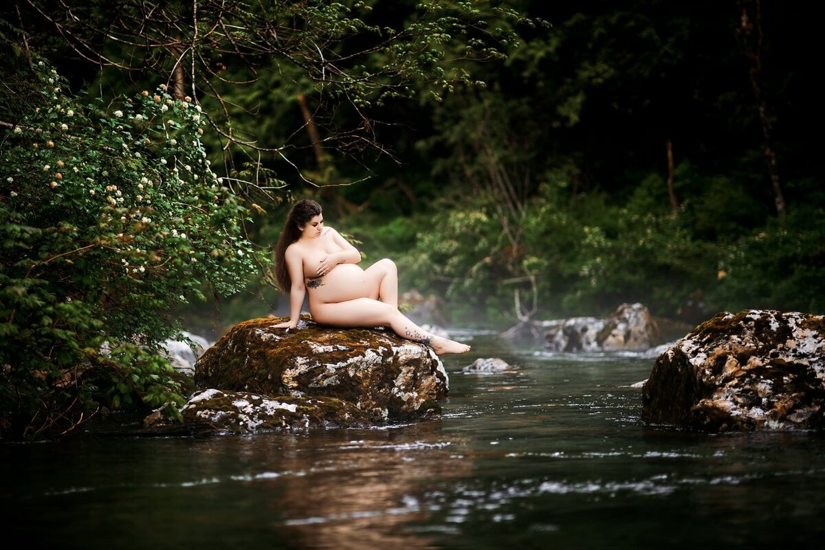 Tasteful nude maternity session with woman sitting on a rock in the Golden Ears Park river