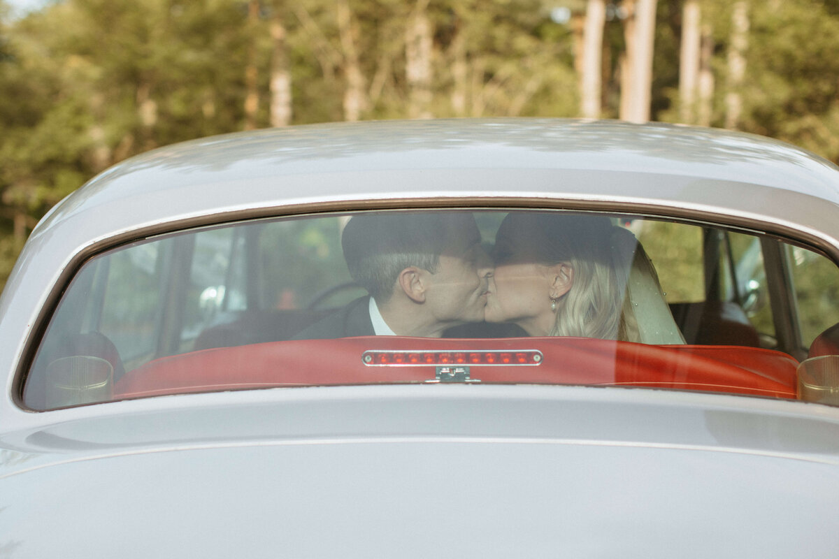 Bride and groom kiss in back of vintage car
