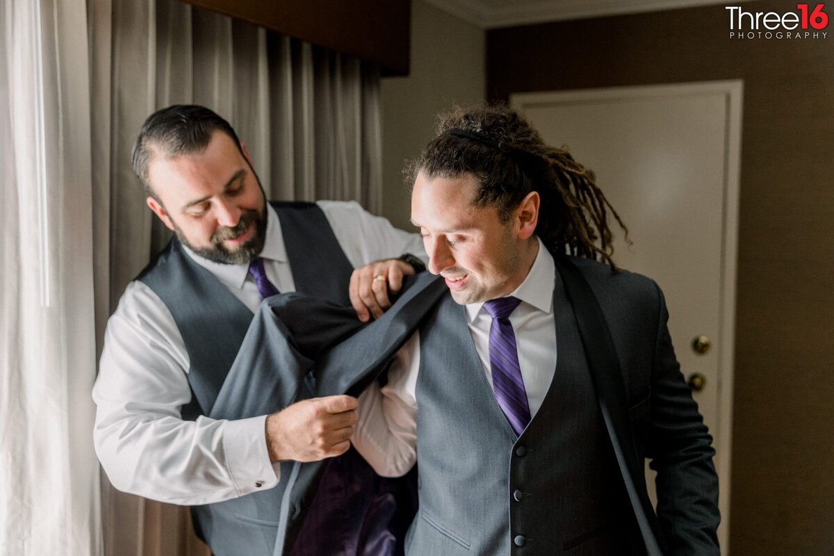 Best Man assists Groom with his suit jacket
