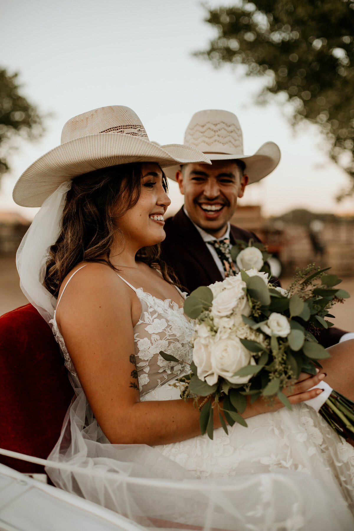 bride and groom sitting in a horse carriage with cowboy hats laughing
