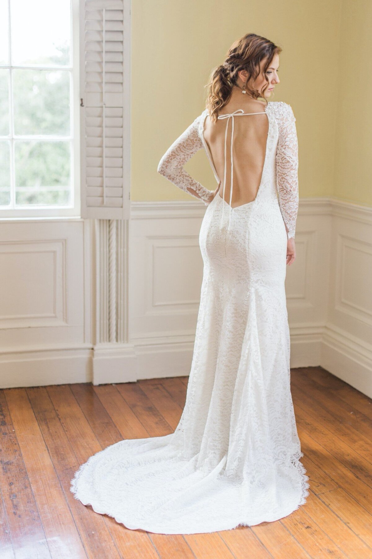 The Hudson bridal style is a low-back lace wedding dress with long sleeves and a scallop edge hem that goes all the way around the train as well.