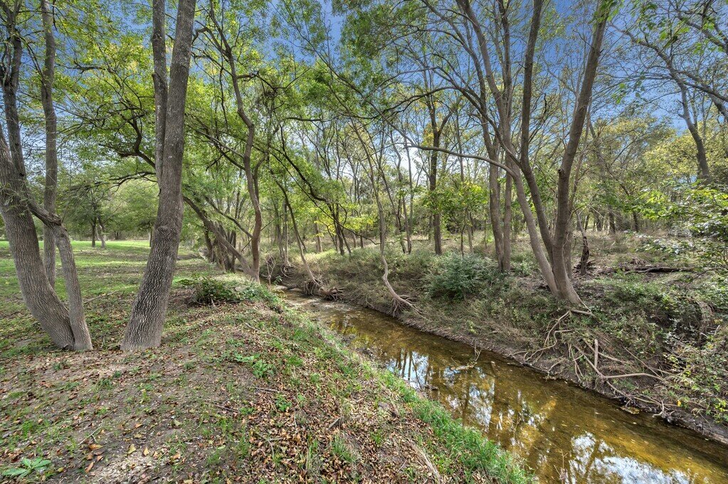 Tree lined creek on the property of this four-bedroom, four-bathroom vacation rental home and guest house with free WiFi, fully equipped kitchen, firepit and room for 10 in Waco, TX.
