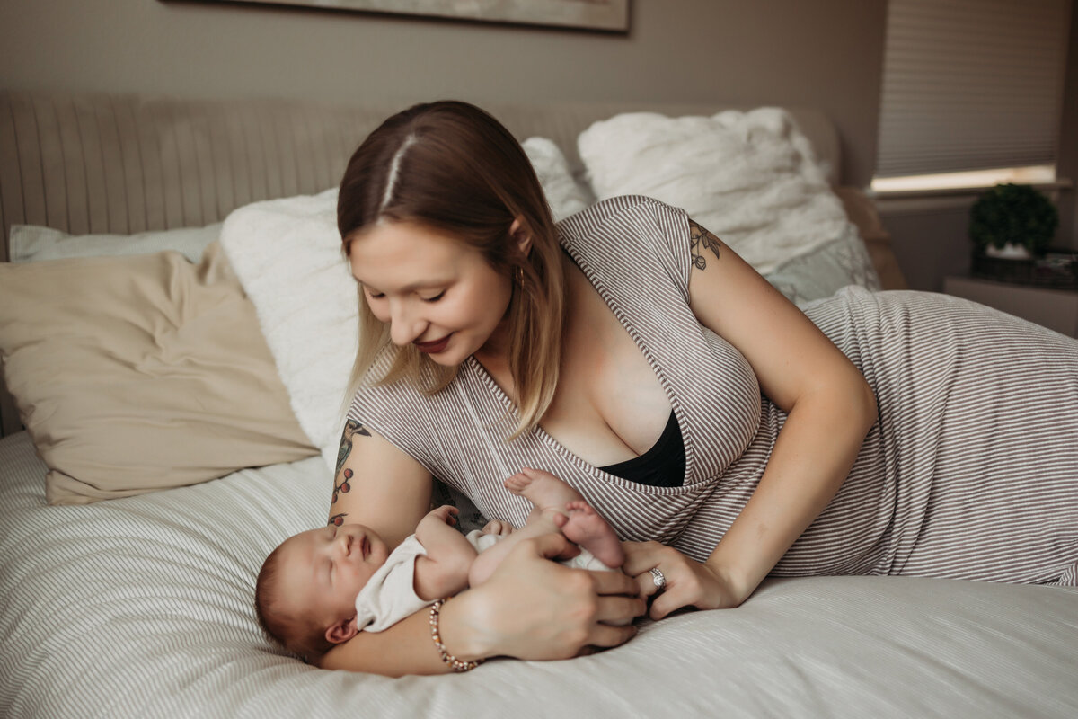 new mom cuddles baby boy while laying on bed in neutral colored master bedroom