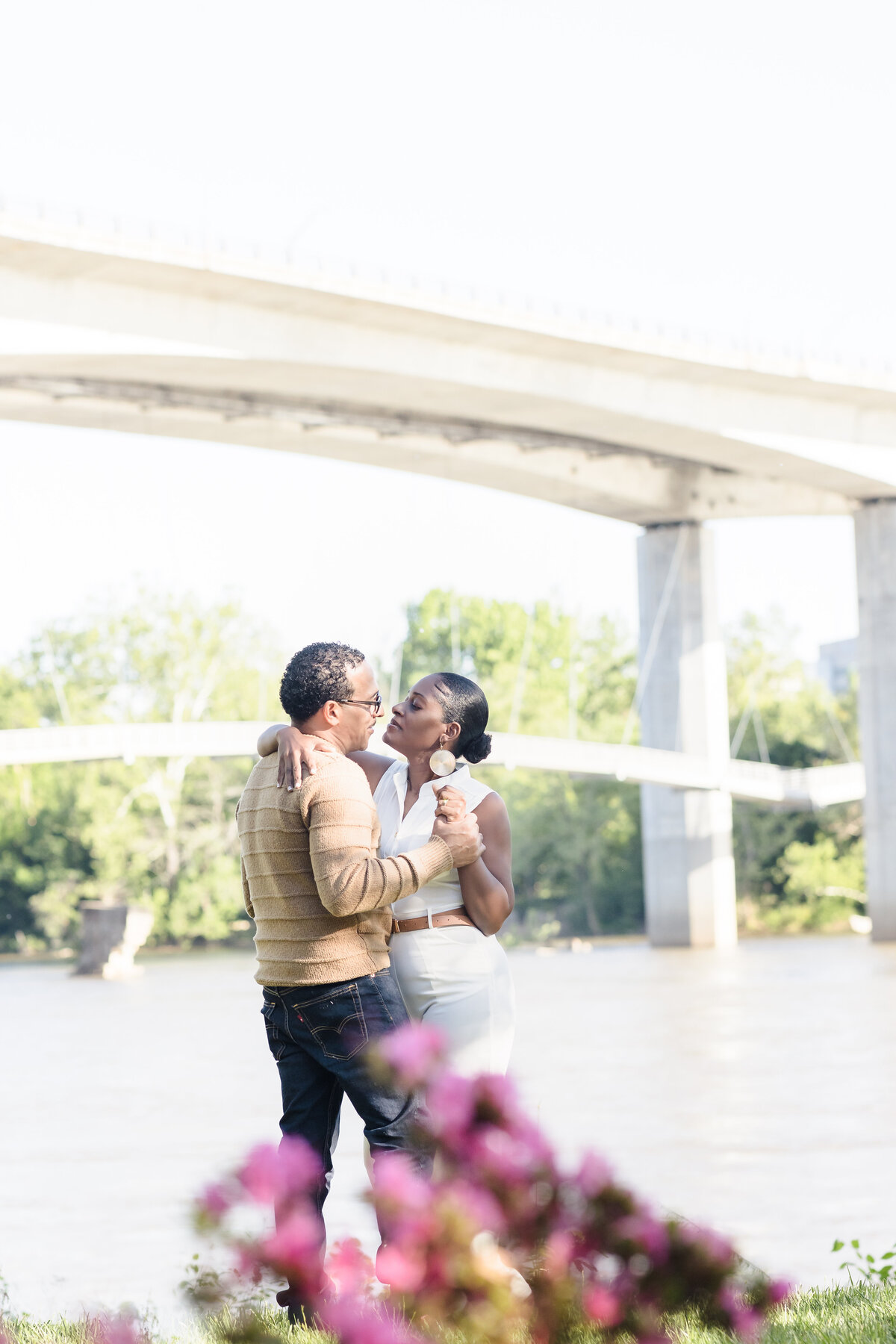 man and woman embrace under bridge by river