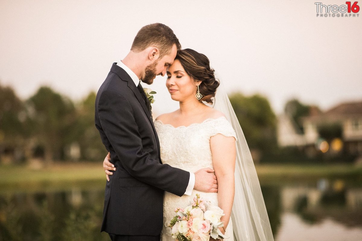 Groom gives his Bride an gentle embrace in front of the golf course pond