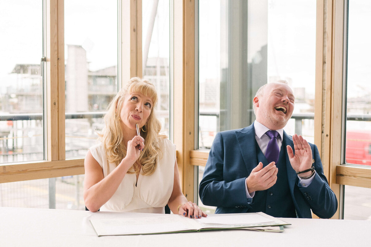 A bride and groom laughing as they sign the marriage registar