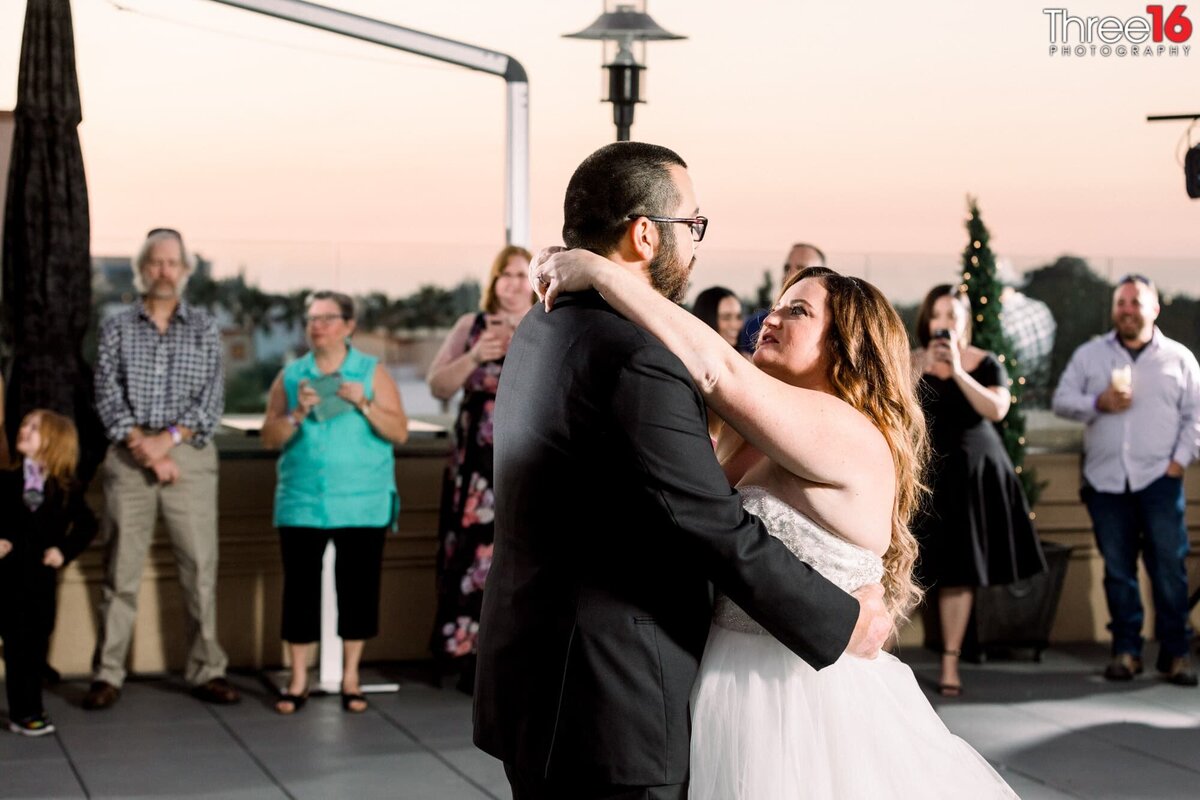 Newly married couple hold each other during their first dance in front of their wedding guests