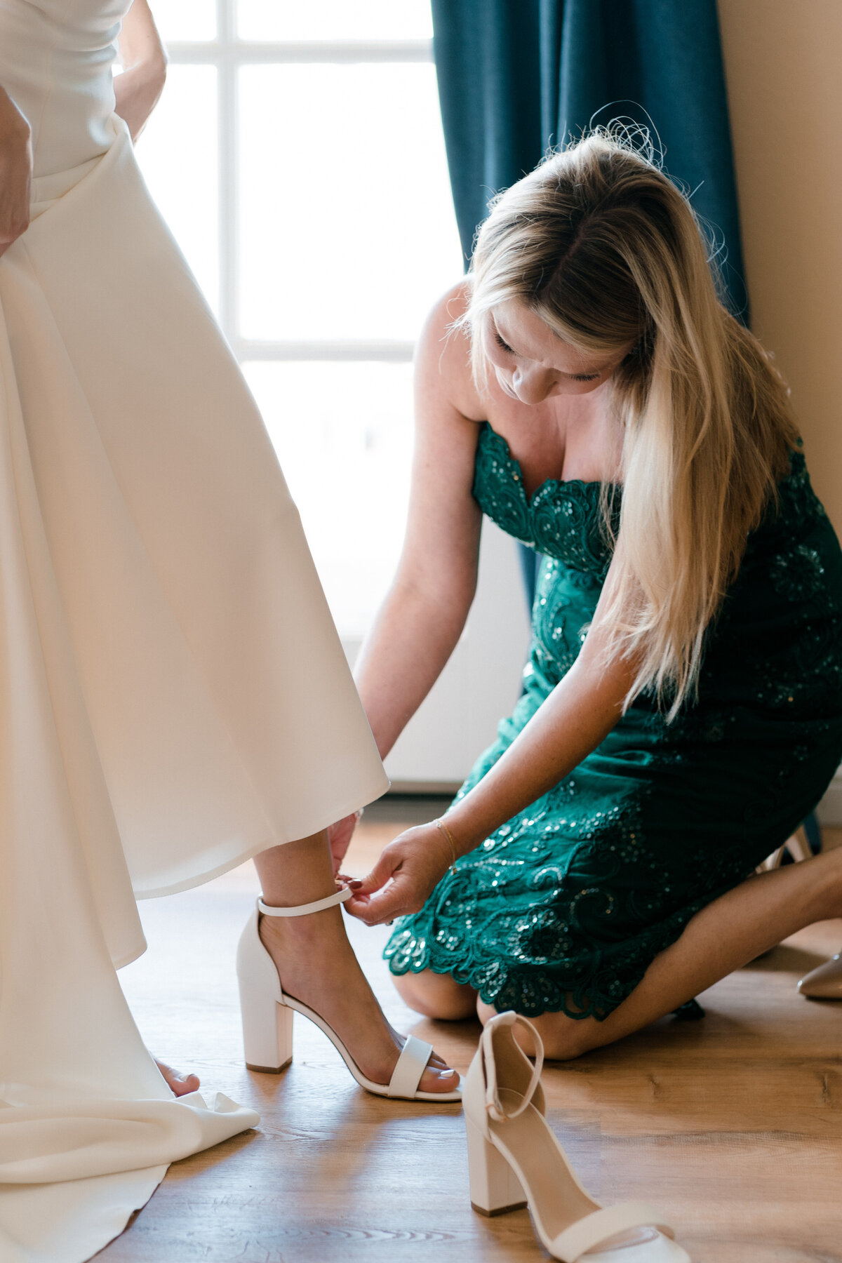 women in a green dress putting on brides white heeled sandal