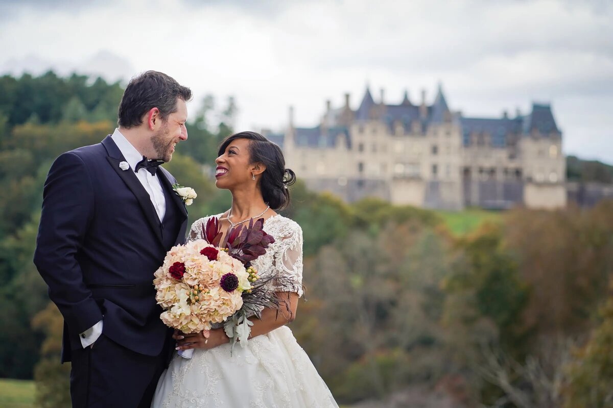 Bride and groom smiling at each other with a historic castle in the background