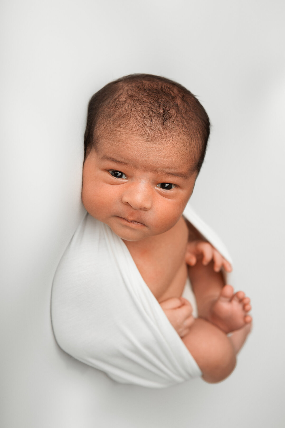 White wrapped studio newborn pose with an awake newborn