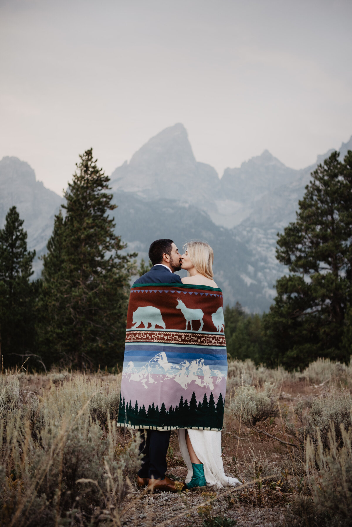 Photographers Jackson Hole capture bride and groom cuddling with blanket kissing
