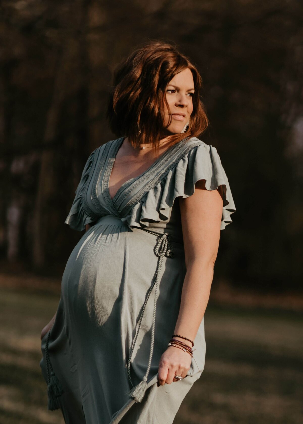 A pregnant woman in a green dress poses gracefully in a field, captured beautifully by a Pittsburgh maternity photographer.