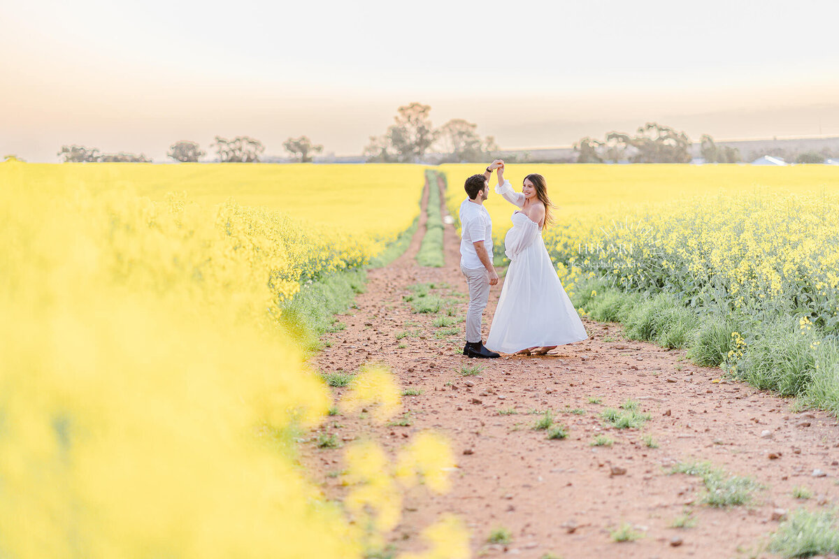 couple walking along canola field in gold coast south australia twirling during maternity photo session by hikari