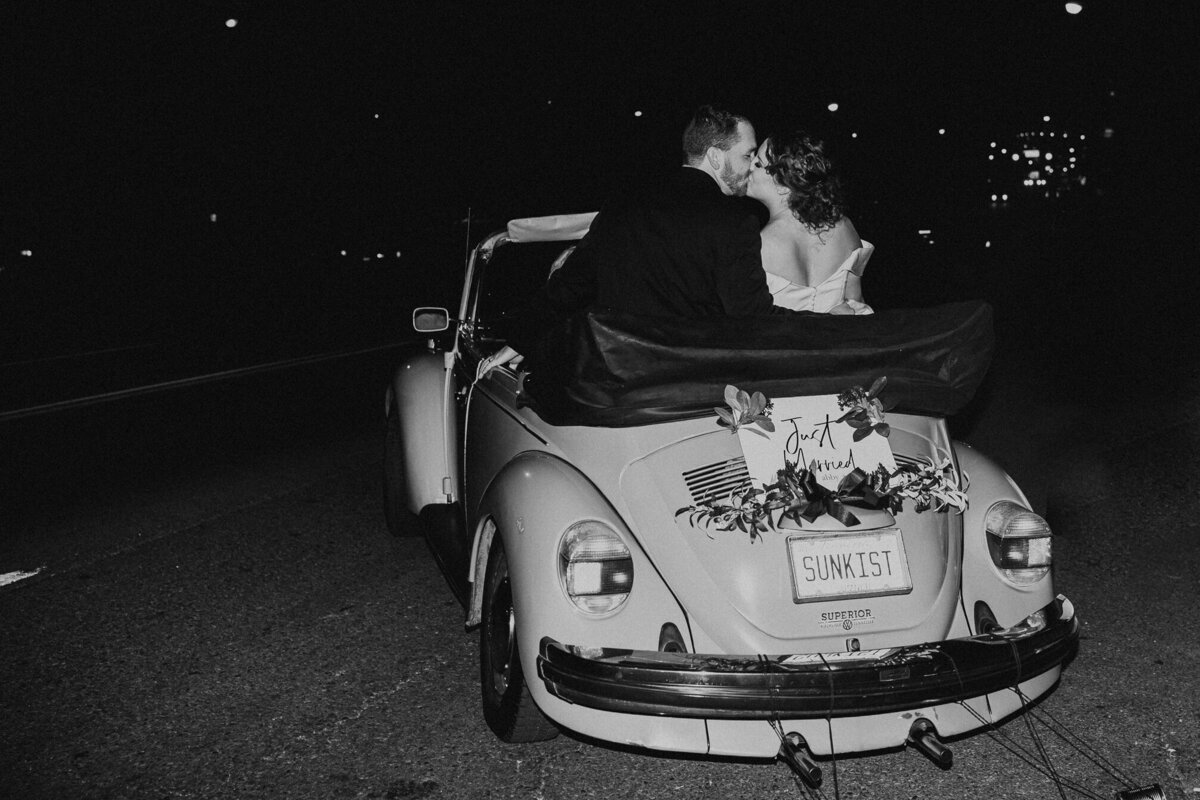 bride and groom kissing during exit in old fashion getaway car