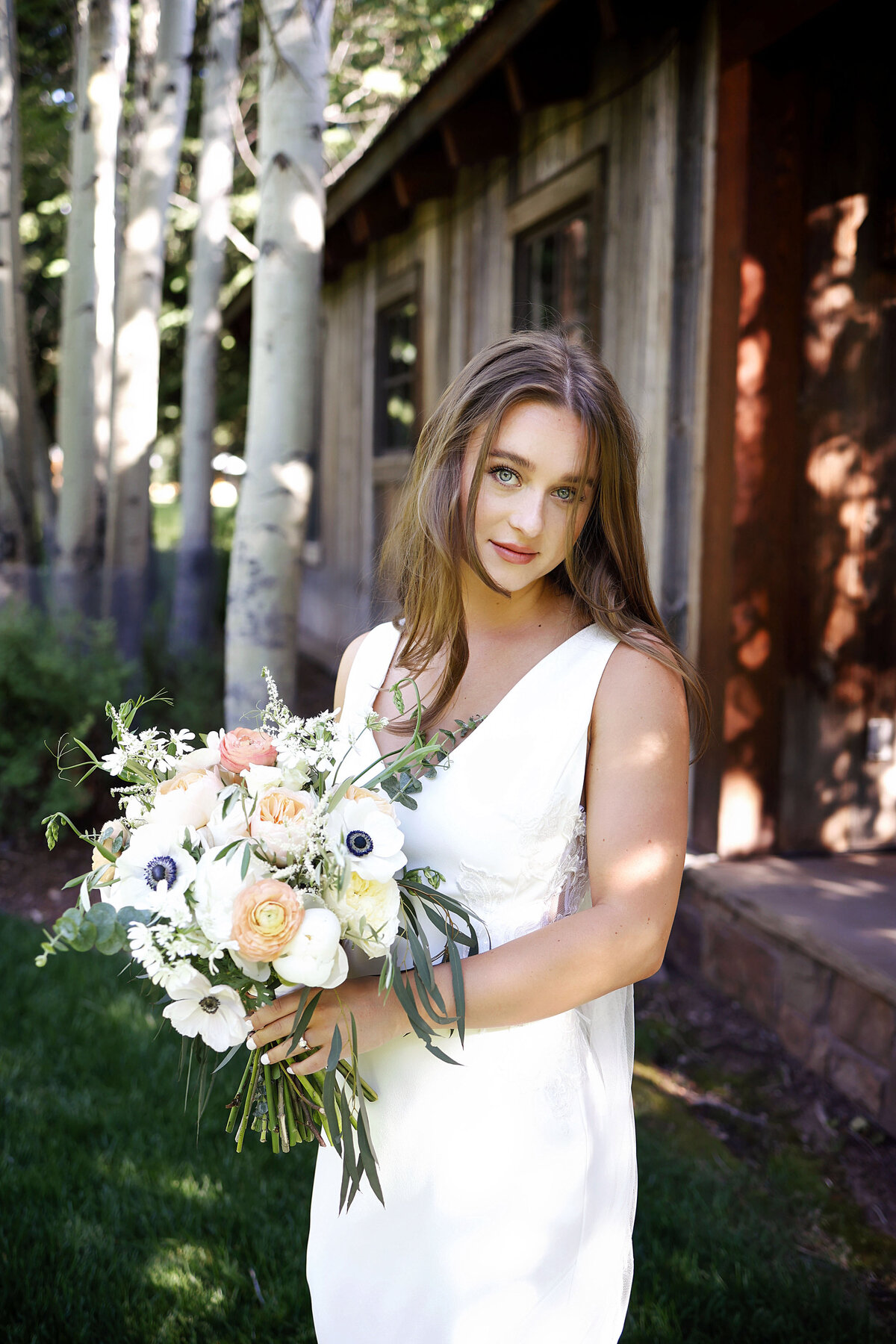 A young beautiful bride, holding her brightly colored bouquet and giving the camera a small smile,