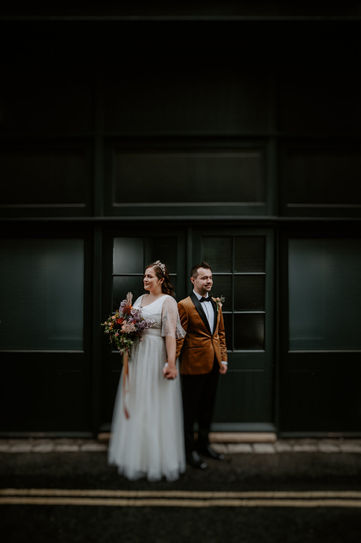 A tilt shift portrait of a wedding couple during their first look. The groom is wearing an orange velvet jacket and the bride is wearing a wedding dress with stars. This was taken in St Andrews Wharf in London. They then went onto getting married at The Asylum in Peckham.