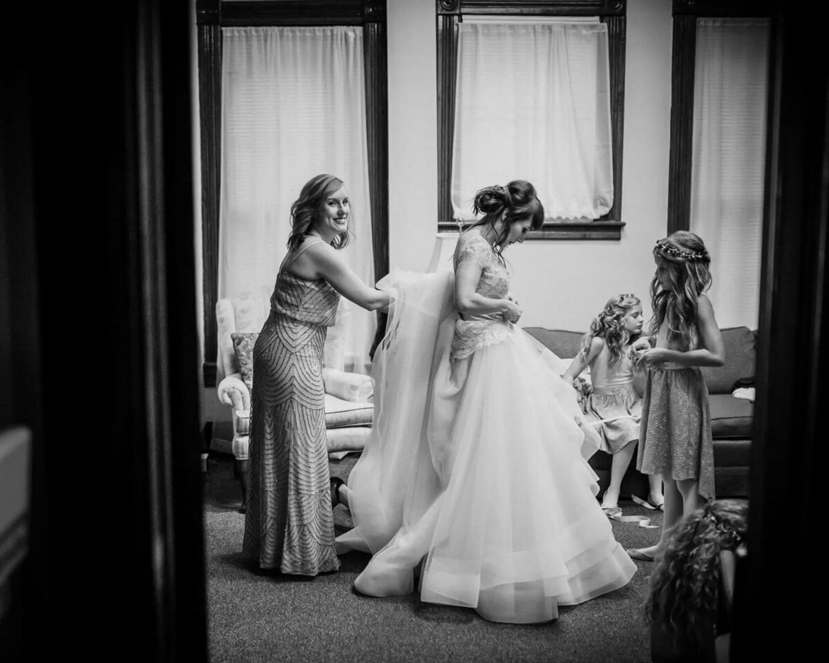 A woman helping a bride put on her dress.